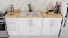 A modern kitchen unit with white cabinets and a wooden countertop, featuring a sink, faucet, and various kitchen accessories. Produktbild-Vorschau
