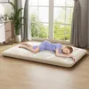 A woman is sleeping on a floor mattress in a bright room with large windows. Náhľad obrázku produktu