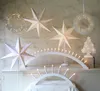A collection of Christmas decorations, including paper stars, a wreath, and candle arches, displayed on a shelf. Podgląd zdjęcia produktu
