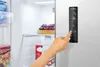 A hand is shown interacting with the digital control panel of a refrigerator. Podgląd zdjęcia produktu