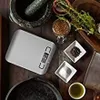 A top-down view of a kitchen scale and ingredients, including herbs, spices, salt, and olive oil. Náhľad obrázku produktu