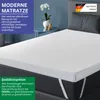 A mattress topper is shown on a bed, with decorative elements and text overlays. Produktbild-Vorschau