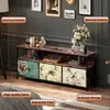 A TV stand with decorative drawers in a room setting, with framed pictures on the wall and a lamp. Podgląd zdjęcia produktu