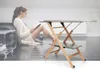 A woman is reading a book while sitting on the floor next to a sofa, with a folding ironing board in the foreground. Voir les images du produit