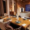 A dining table set for a meal in a modern, rustic-style dining room with exposed brick walls and large windows. Produktbild-Vorschau