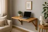 A wooden wall-mounted folding desk with a laptop and a plant on it, next to a sofa and a side table with a lamp. Produktbild-Vorschau
