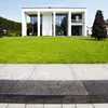 A modern white house with a large green lawn and a paved walkway in the foreground. Produktbild-Vorschau