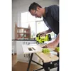 A man is using a cordless jigsaw to cut a piece of wood on a workbench. There is a dollhouse in the background. Produktbild-Vorschau