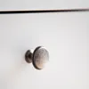 A close-up shot of a single silver drawer knob on a white surface. Produktbild-Vorschau