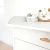 A close-up view of a white changing table with a wooden drawer handle and a small basket with baby items. Podgląd zdjęcia produktu