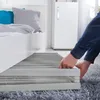A person's hands are shown adjusting a slatted bed base under a white bed frame. Pillows are visible on the bed. Produktbild-Vorschau
