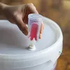 A hand holding a fermentation airlock over a white bucket lid. Produktbild-Vorschau