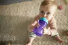 A baby sitting on a rug and drinking from a sippy cup. Voir les images du produit