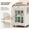 A close-up view of a white kitchen cart with a glass door, showcasing its interior and adjustable shelves, with text overlays highlighting features. Podgląd zdjęcia produktu