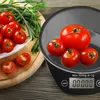 A digital kitchen scale with tomatoes and herbs on a wooden surface. Produktbild-Vorschau