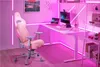 A gaming setup with a pink gaming chair, desk, computer, and laptop, illuminated by pink neon lights. Produktbild-Vorschau