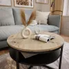 A round coffee table with a wooden top and black metal frame, placed in a living room setting with a sofa and rug. Náhled obrázku produktu
