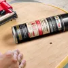 A hand is shown near a spray can of adhesive on a wooden surface, with a staple gun in the background. Produktbild-Vorschau