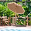 A patio umbrella is set up next to a swimming pool and wooden furniture on a deck, surrounded by lush greenery. Produktbild-Vorschau