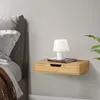 A floating nightstand with a drawer, a book, and a lamp next to a bed. Anteprima dell’immagine prodotto