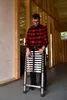 A man is holding a folded telescopic ladder indoors, possibly during a construction or renovation project. Produktbild-Vorschau