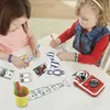 Two young girls are sitting at a table, engaged in an activity with a VTech Kidizoom Print Cam and various craft supplies. Anteprima dell’immagine prodotto