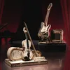 A diorama of musical instruments, including a violin and an electric guitar, with a piano and stage curtains in the background. Voir les images du produit