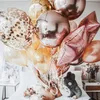 Ein großer Strauß aus Rosenquarz-, Gold- und Konfetti-gefüllten Luftballons, gehalten von einer Person, die auf einem Bett sitzt Náhled obrázku produktu