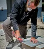 A person is using a power tool to cut a tile on a construction site. Produktbild-Vorschau