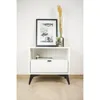 A white bedside table with a drawer and an open shelf, decorated with a framed picture and a vase with dried grass. Produktbild-Vorschau