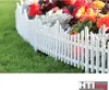 A white picket fence bordering a flower bed with green grass in the foreground. Produktbild-Vorschau