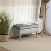 A gray upholstered storage bench with wooden legs is placed in a room with paneled walls and a coat rack. Náhled obrázku produktu