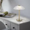 A table lamp with a white marble-like shade and a gold base sits on a white dresser next to an open magazine. Voir les images du produit