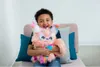 A young boy is sitting on a chair, holding a colorful stuffed toy. Voir les images du produit