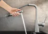 A hand is holding a pull-out spray faucet, with water spraying out. Produktbild-Vorschau