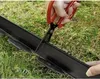 Hands using scissors to cut a black garden edging strip on grass. Podgląd zdjęcia produktu