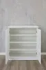 An open white cabinet with shelves against a textured gray wall and wooden floor. Produktbild-Vorschau
