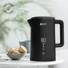 A black electric kettle is displayed on a white table, with a small bowl of cookies and a mug in the background. Produktbild-Vorschau