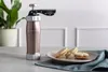 A rose gold biscuit press sits on a table next to a plate of cookies, with a plant in the background. Anteprima dell’immagine prodotto