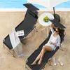 Two black lounge chairs are set up on a sandy area next to a swimming pool. One chair has a gray blanket and an open book on it. The other chair has a woman relaxing on it, wearing sunglasses and a light blue shirt. A small white table with fruit and a whi Náhled obrázku produktu