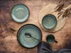A rustic table setting with ceramic plates, bowls, and a mug, accented by dried plant sprigs. Produktbild-Vorschau