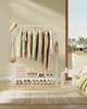 A room with a clothing rack filled with clothes, shoes on the floor, and a bed in the background. Produktbild-Vorschau