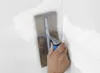 A hand is using a trowel to apply plaster to a wall corner. Produktbild-Vorschau