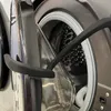 A close-up view of a washing machine door and drum, with a black magnetic door holder attached to the door. Produktbild-Vorschau