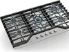 A close-up, angled view of a stainless steel gas cooktop with five burners, four of which are lit with blue flames. Náhľad obrázku produktu