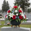 A floral arrangement in a black pot with wooden legs sits on a gravestone in a cemetery. Podgląd zdjęcia produktu
