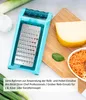 A grater attachment for a kitchen appliance is shown on a wooden cutting board next to cheese and grated carrots. Leeks and garlic are in the background. Produktbild-Vorschau