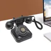 A vintage black rotary phone is placed on a white surface next to a laptop and a notebook, with a brown background behind it. Podgląd zdjęcia produktu