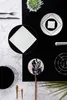 A flat lay arrangement of black and white tableware items on a black and marble background, with a plant and decorative elements. Produktbild-Vorschau