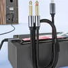 A black audio cable with two 6.35mm jack connectors and a USB-C connector is shown connected to a smartphone, which is placed on a black box. In the background, a speaker is visible. Anteprima dell’immagine prodotto